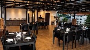 A restaurant with multiple dining tables, black chairs, and a bar area with a counter and stools. - Hotel O Seagull (Port-Blair)