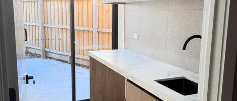 A modern kitchen with wooden cabinets, a marble countertop, and a black sink.