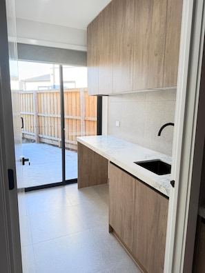 A modern kitchen with wooden cabinets, a marble countertop, and a black sink.