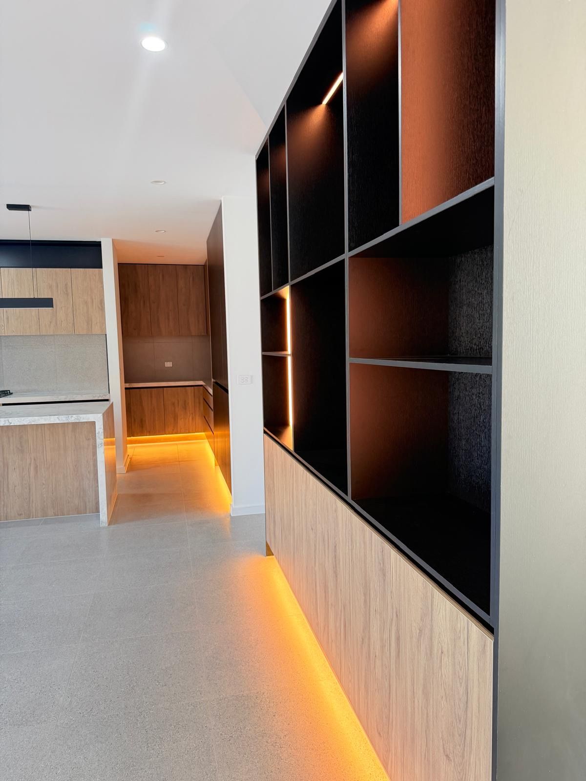A modern interior with a kitchen area, built-in shelving, and a hallway.