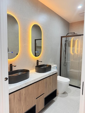 A modern bathroom with two sinks, a toilet, and a shower enclosure.