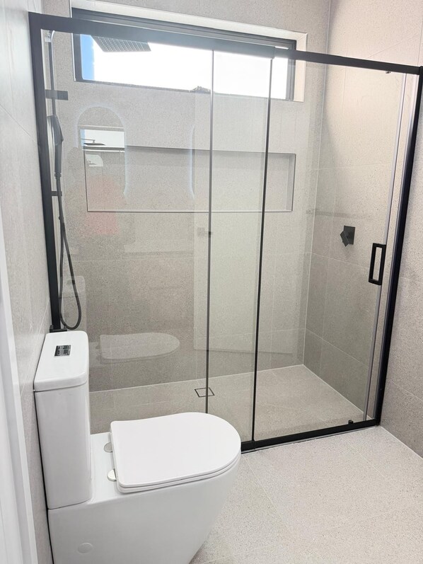 A modern bathroom with a glass-enclosed shower, a white toilet, and a small sink.