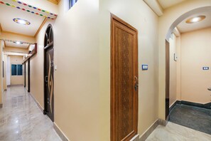 Corredor de hotel com porta de madeira, piso de azulejos e teto com iluminação embutida.
