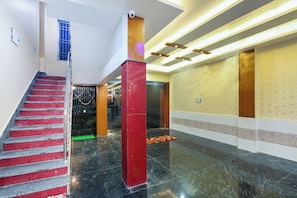 Um hall de hotel com piso de mármore, escadaria e balcão de recepção.