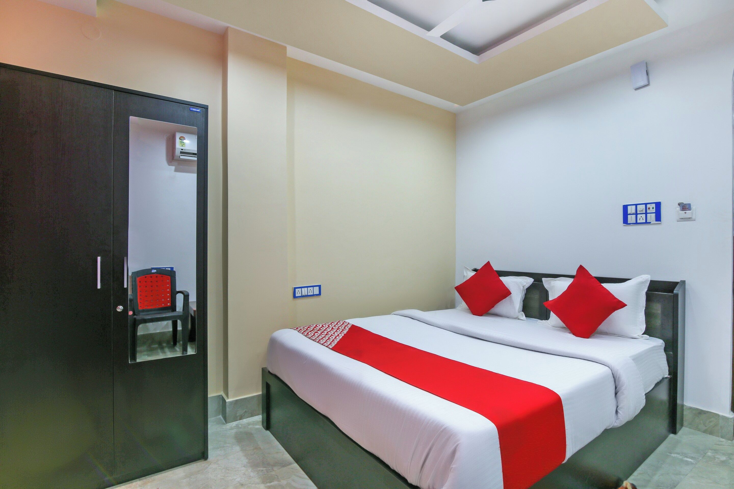 Quarto de hotel com cama, guarda-roupa, cadeira e luminária de teto.