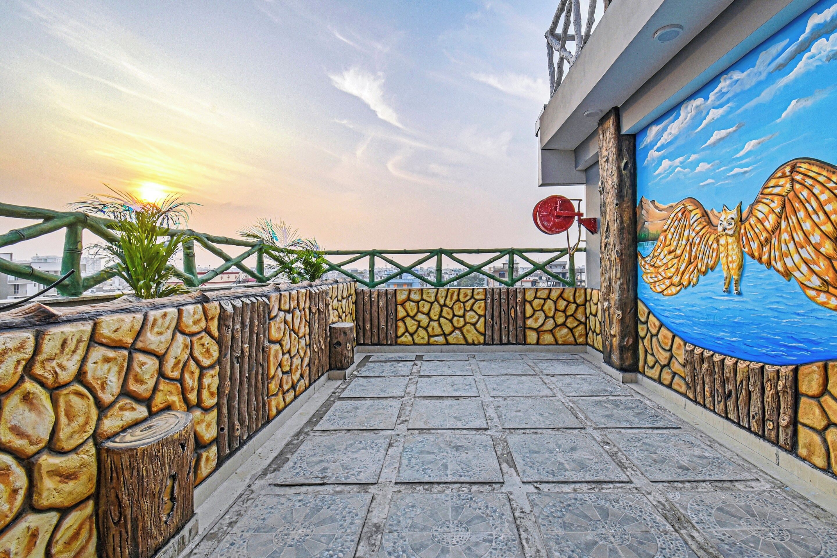 Una terraza en la azotea con un muro de piedra, un mural de un búho y vistas del atardecer.