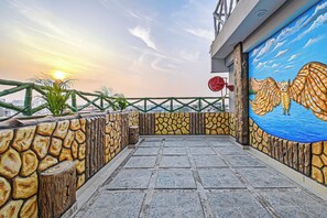 Una terraza en la azotea con un muro de piedra, un mural de un búho y vistas del atardecer.