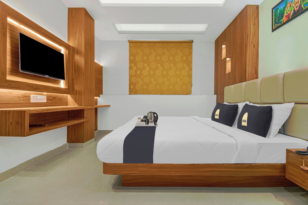 Une chambre d’hôtel moderne avec un grand lit, une tête de lit en bois, un téléviseur à écran plat fixé au mur et une petite table avec une bouilloire et des tasses.