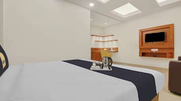A hotel room with a bed, a television mounted on the wall, a small kitchen area with a kettle, and a tray with breakfast items.