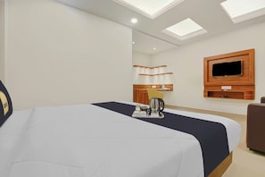 Habitación de hotel con cama, televisor montado en la pared, pequeña cocina con hervidor y bandeja con artículos de desayuno.