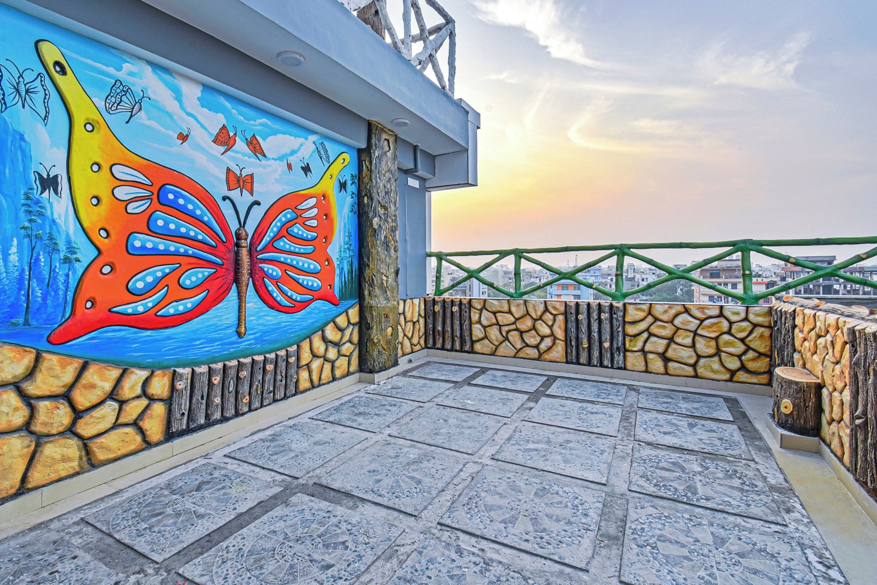 Una terraza en la azotea con un mural de mariposas de colores, paredes de piedra y barandilla de metal verde.