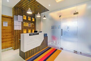 Un mostrador de recepción con un letrero que dice 'TOWN HOUSE OAK Hotel Holiday Grand' y un interior moderno con paneles de madera e iluminación colgante.