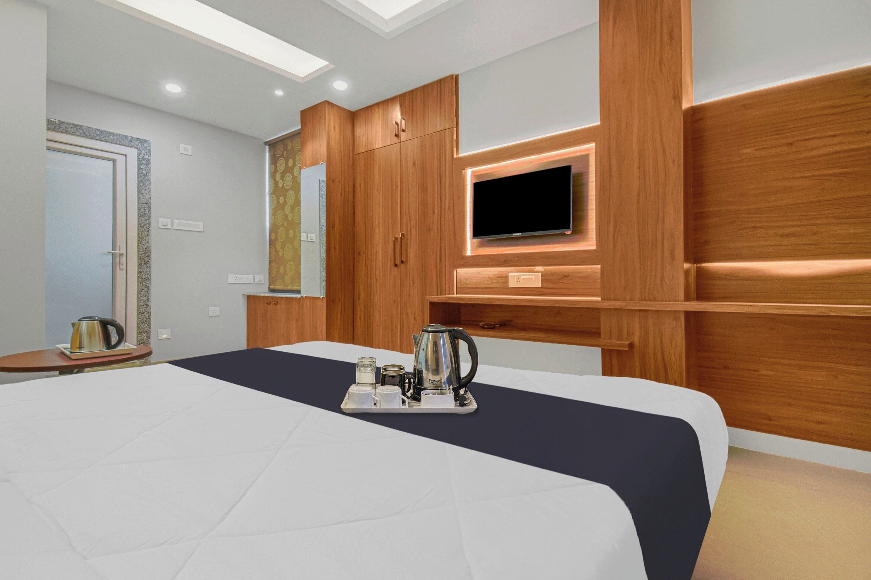 Una habitación de hotel moderna con una cama grande, un televisor de pantalla plana montado en la pared, paneles de madera y una bandeja con hervidor y tazas.