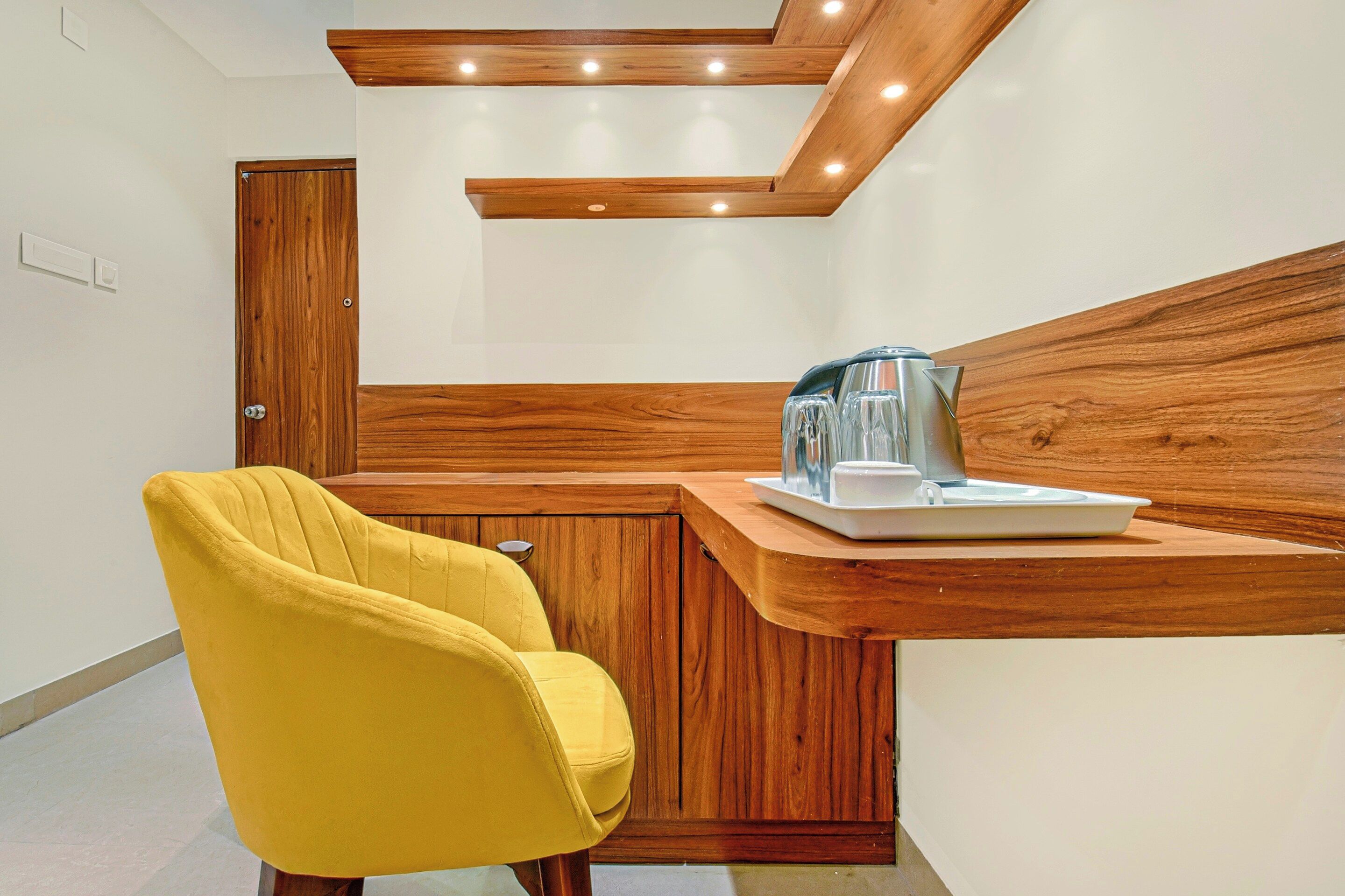 A modern kitchen with wooden cabinetry, a yellow chair, and a coffee maker on the counter.