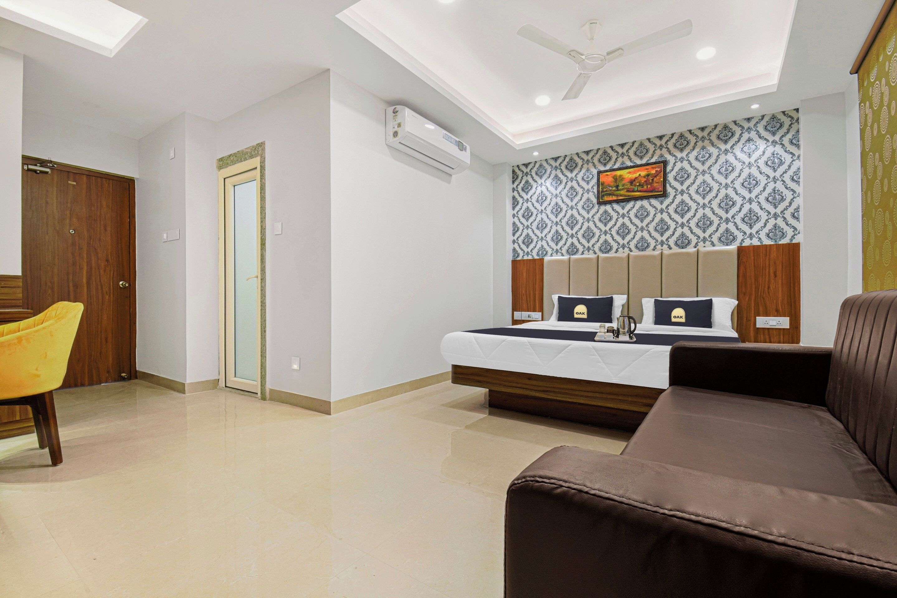 A hotel room with a bed, a sofa, a chair, and a ceiling fan.