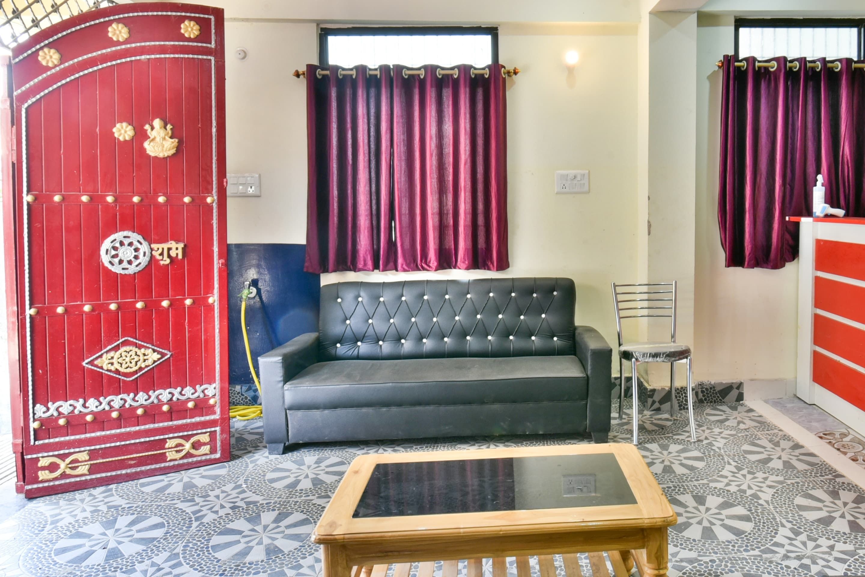 Una sala de estar con un sofá, una mesa de centro de vidrio, una puerta decorativa roja y cortinas moradas.