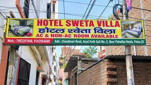 Une enseigne d’hôtel indiquant les chambres climatisées et non climatisées, les numéros de téléphone et l’adresse.