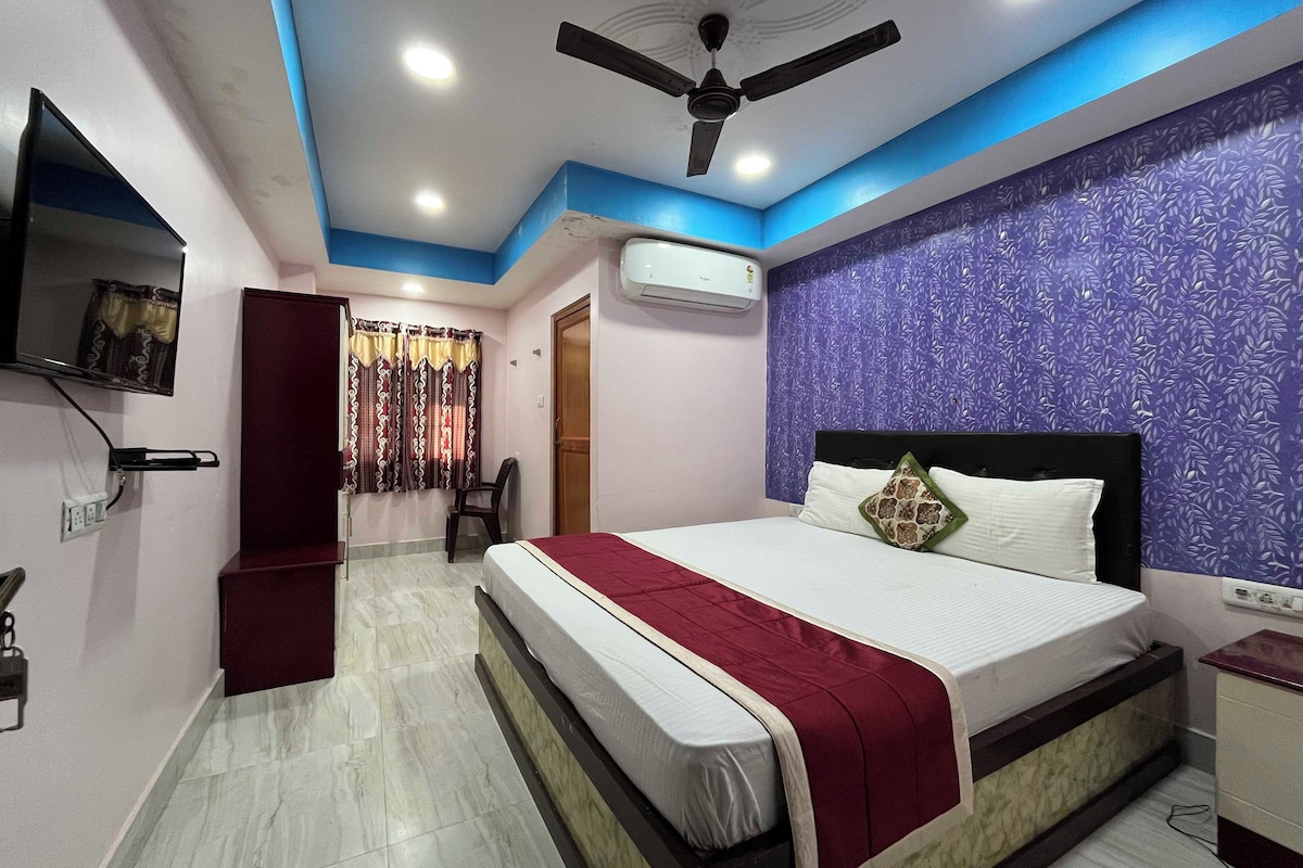A bedroom with a bed, a ceiling fan, an air conditioning unit, and a television mounted on the wall.