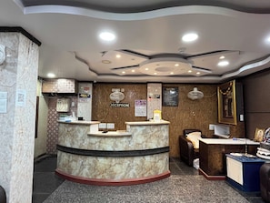 A reception area with a marble counter, a reception desk, a wall-mounted fan, and a framed picture. - Hotel O Shree Karpagrram Dreams. (Port-Blair)