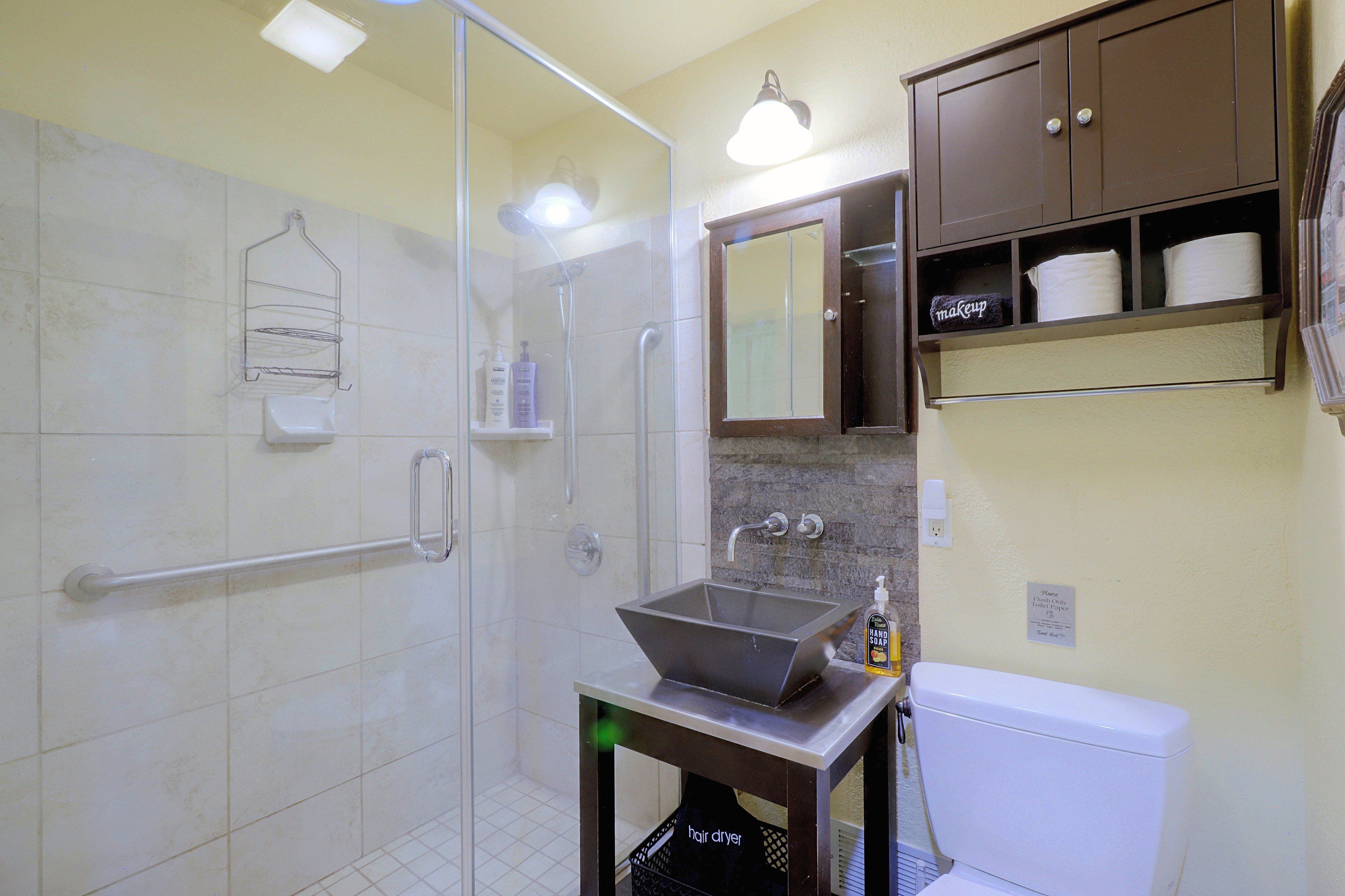 Un baño con cabina de ducha de vidrio, un lavamanos con dispensador de jabón y un inodoro.
