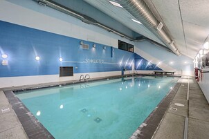 Ein Schwimmbecken mit klarem Wasser, umgeben von einer blauen und weißen Fliesenwand, ausgestattet mit Sicherheitsvorkehrungen wie Rettungsringen und einer Poolleiter.