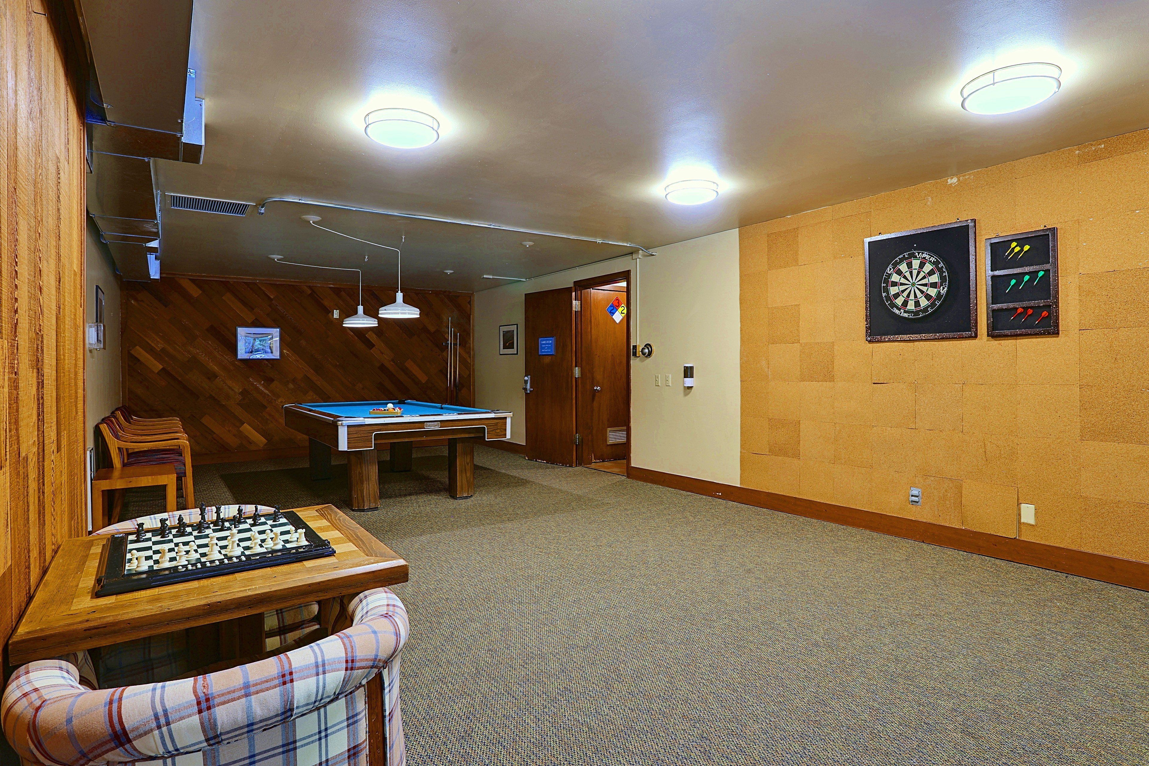 A room with a pool table, a dartboard, and a chess table.