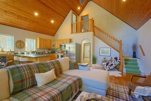 A spacious living area with a high ceiling, a kitchen in the background, and a staircase leading to an upper level.