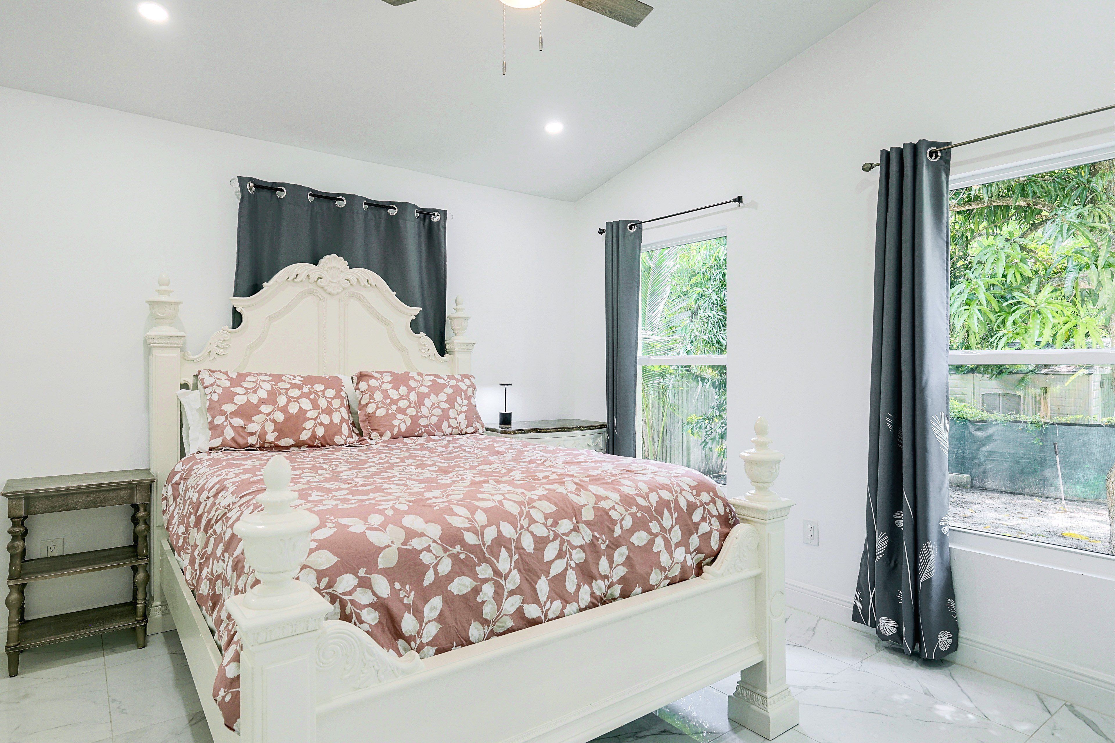 A bedroom with a bed, a nightstand, a window with curtains, and a view of greenery outside.