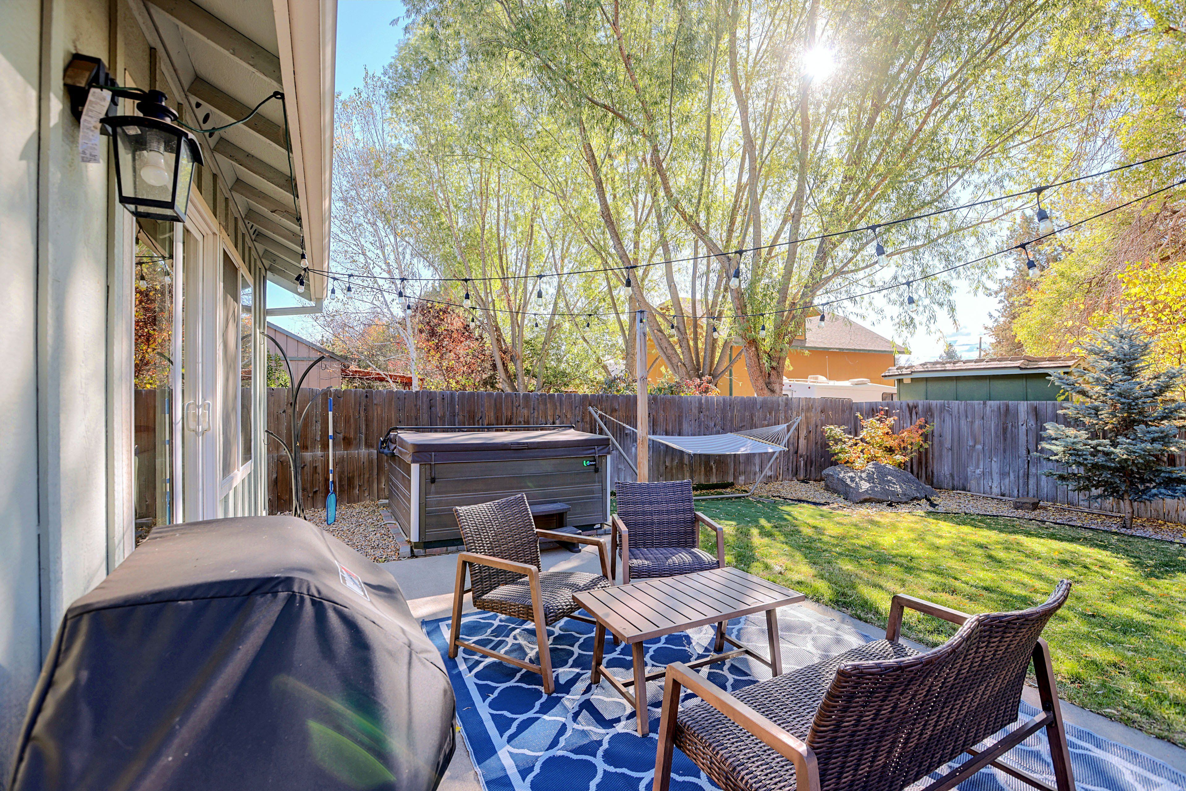 An outdoor patio with a grill, seating area, and a wooden fence.