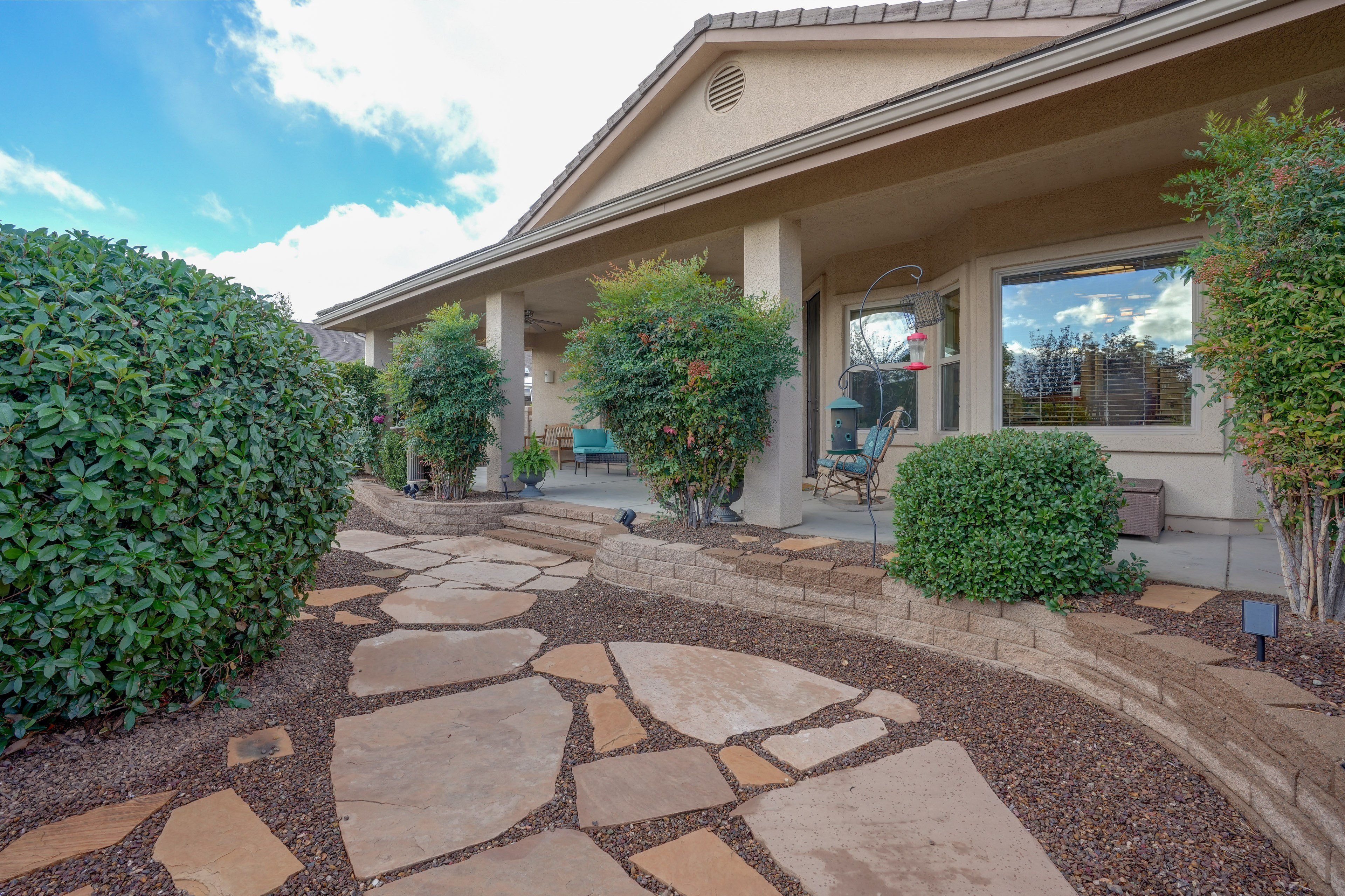 A residential building with a stone pathway leading to the entrance, surrounded by well-maintained hedges and a patio area with outdoor furniture.