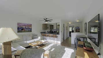 Una sala de estar moderna con un sofá, una mesa de centro y un televisor. Cuenta con una zona de cocina con barra y sillas.
