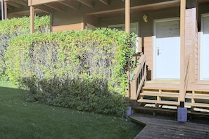 A wooden deck leading to a white door, surrounded by dense green foliage. - Walk to Snow King & Jackson Town Square! Cozy Unit (Jackson)