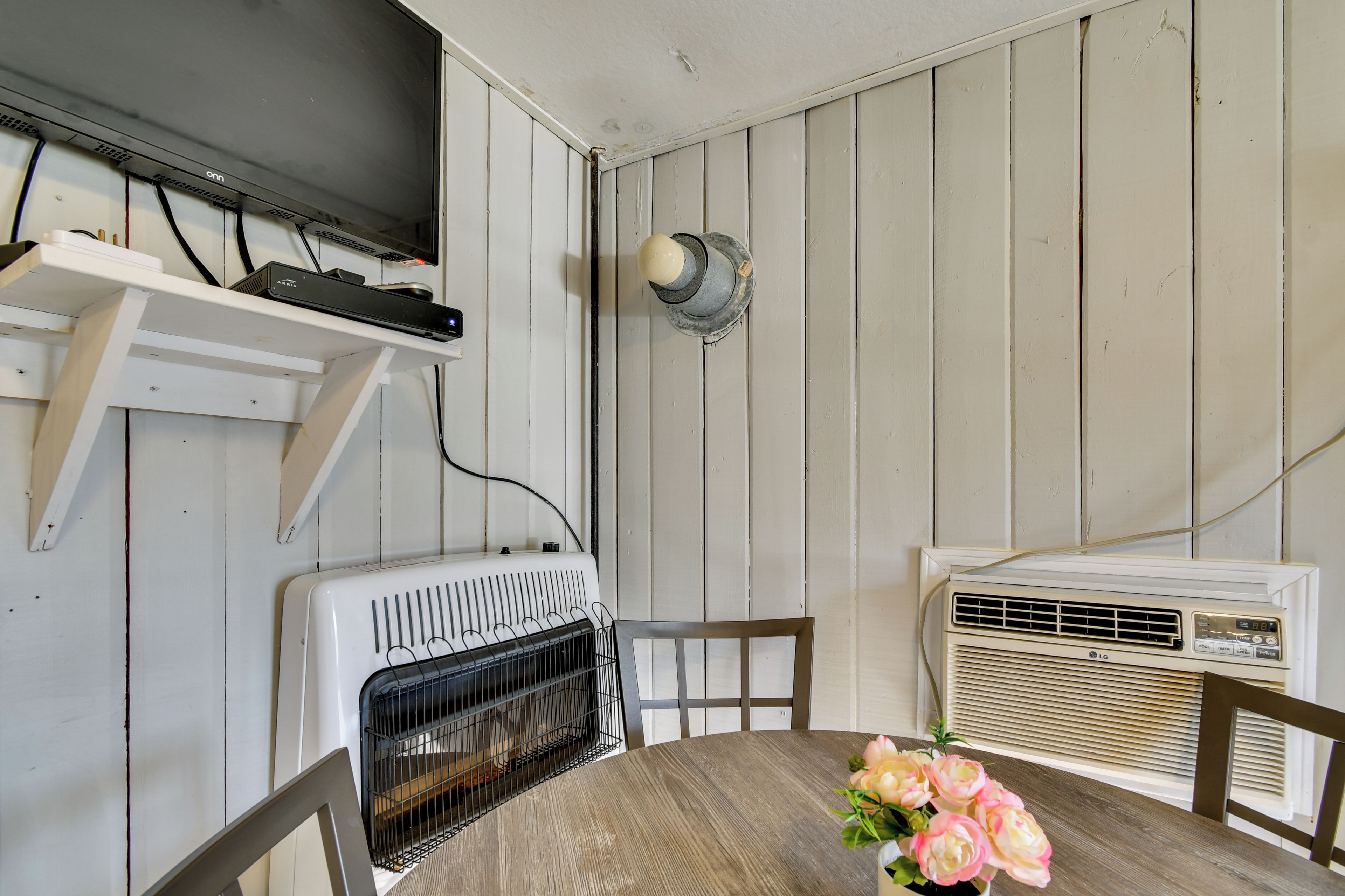 A room with a wooden wall, a white radiator, a television on a shelf, and a table with a flower vase.