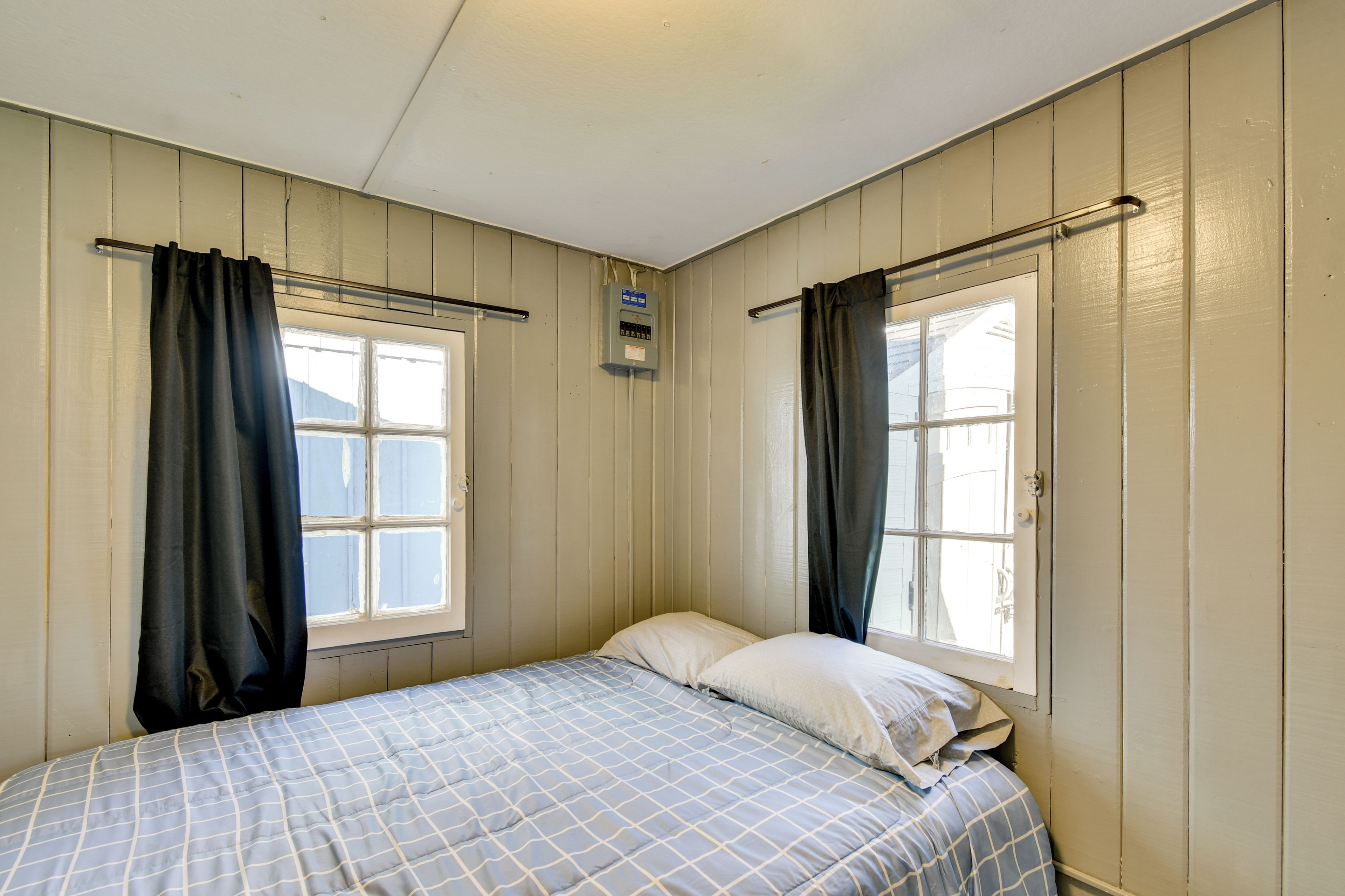 A single bed in a room with two windows, each with a curtain.
