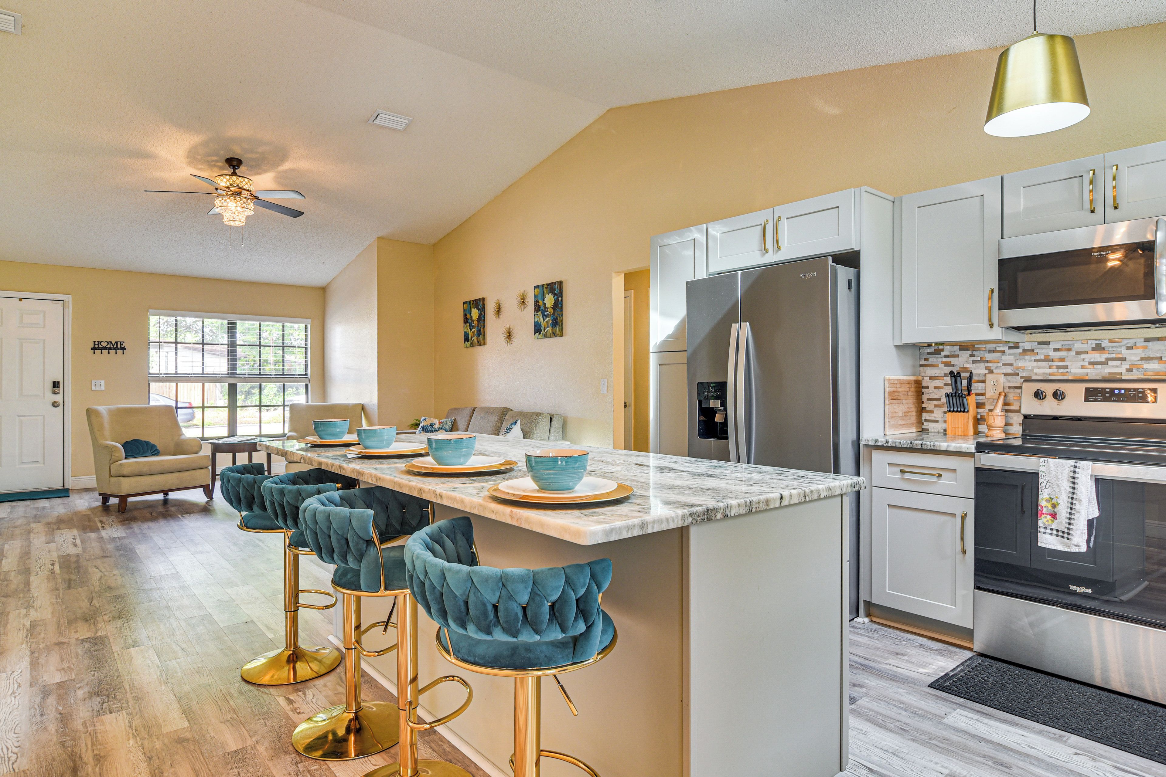 A modern kitchen with a central island, bar stools, a refrigerator, and a microwave.