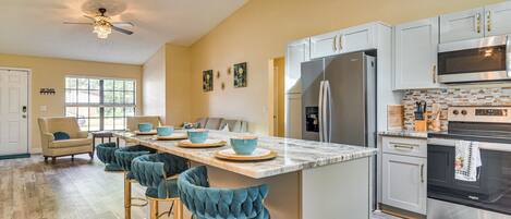 A modern kitchen with a central island, bar stools, a refrigerator, and a microwave.