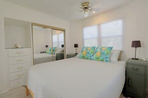 Quarto com cama grande, guarda-roupa, mesa de cabeceira, espelho e ventoinha no teto.