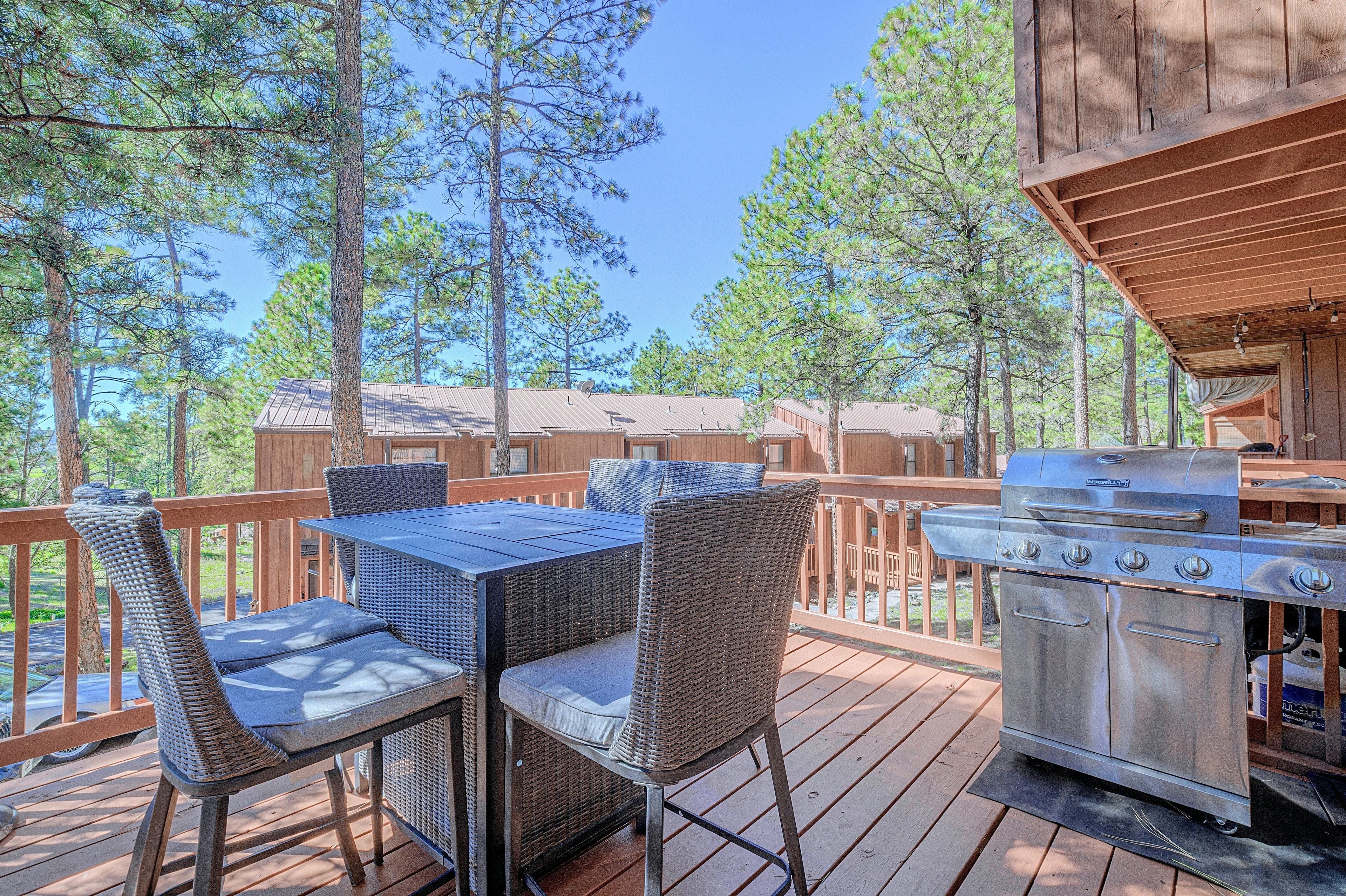 An outdoor deck with a table and chairs, a grill, and a view of surrounding trees.