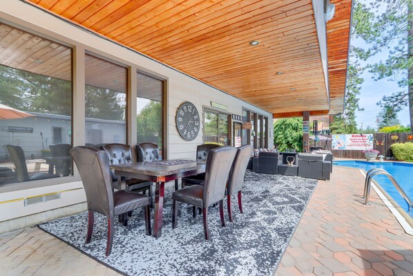 An outdoor patio with a pool, a dining table with chairs, and a clock on the wall.