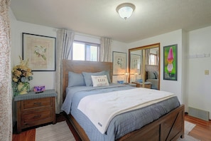 A bedroom with a bed, bedside tables, a dresser, a window with curtains, and wall-mounted artwork.
