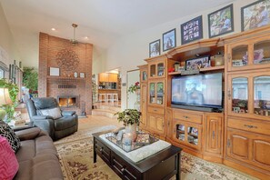 A spacious living room with a fireplace, comfortable seating, a television, and a wooden entertainment center.