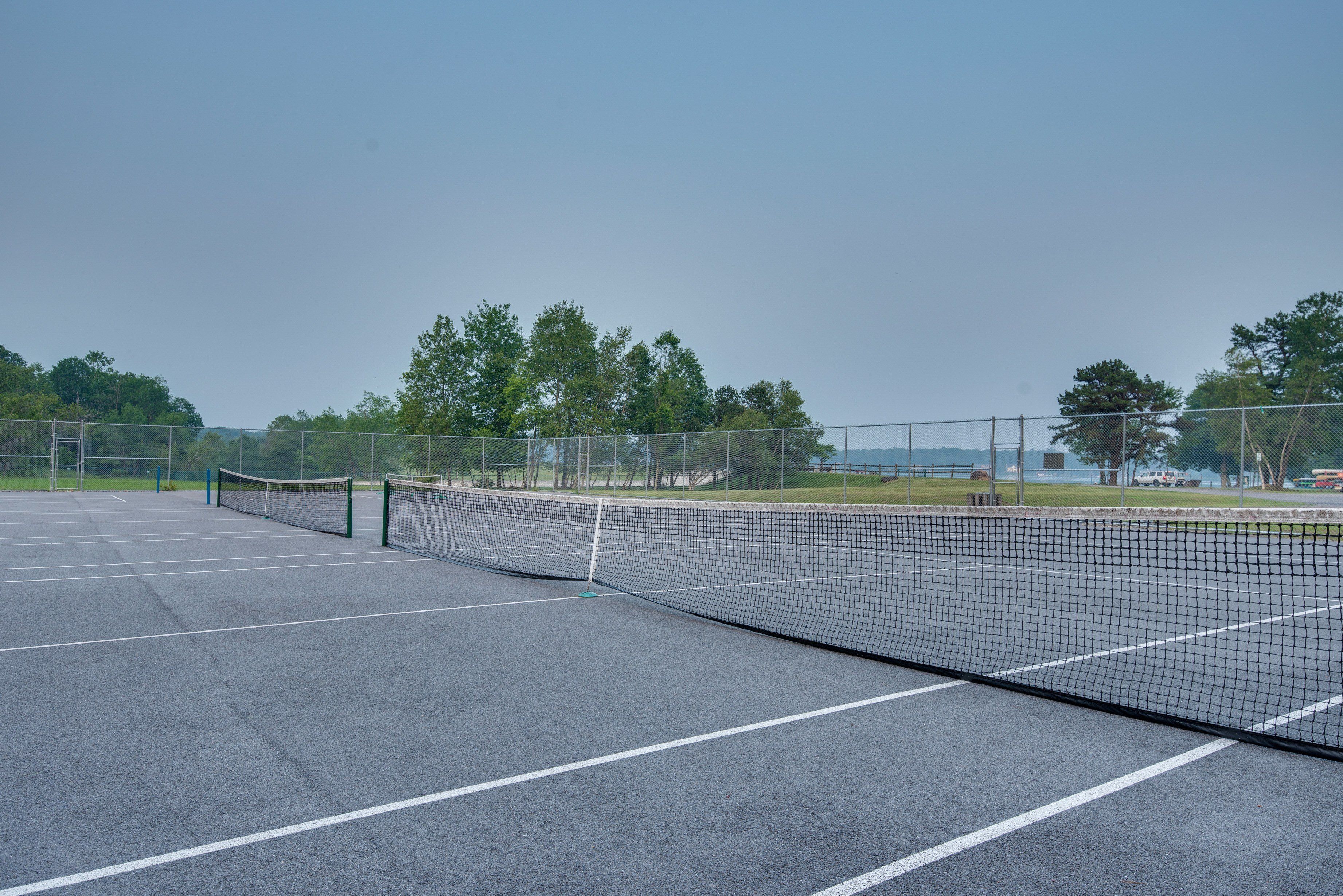 An outdoor tennis court with a net, surrounded by a fence and trees.