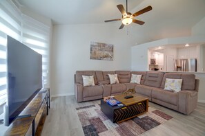 A modern living room with a sectional sofa, a flat-screen TV, a ceiling fan, and a kitchen in the background. - The Boise Retreat Spacious Home, Game Room! (Boise)