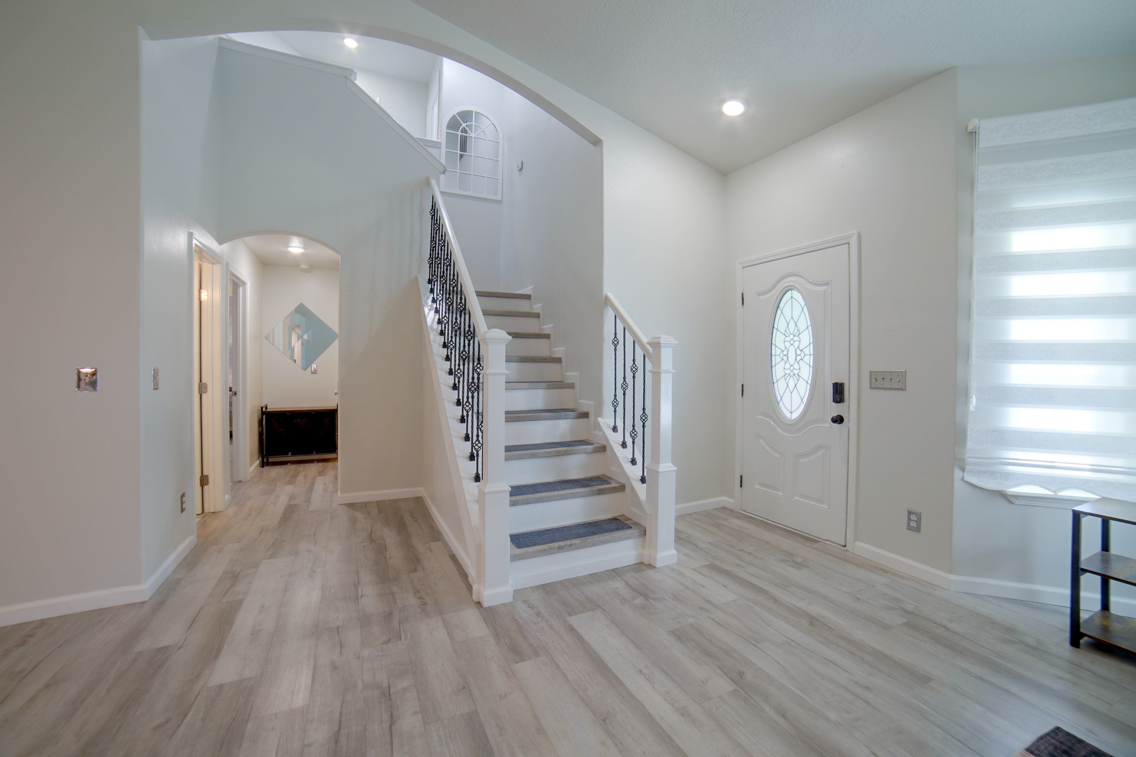 A spacious hallway with a wooden floor, a white staircase with black railings, and a door with a decorative glass panel.