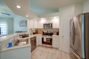 Una cocina compacta con muebles blancos, un refrigerador de acero inoxidable, un microondas y una estufa.
