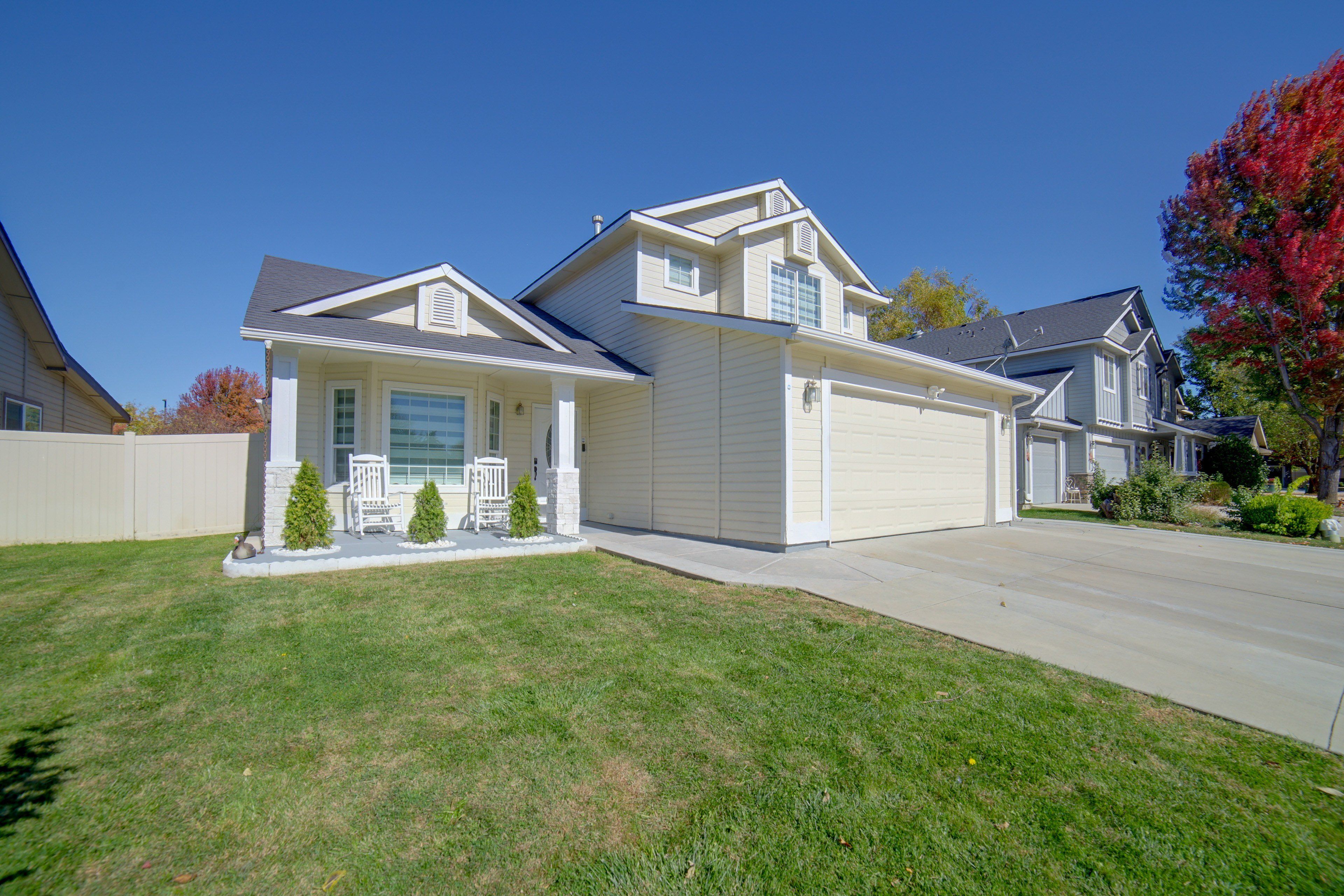 A two-story residential house with a garage, a front porch with a bench, and a well-maintained lawn.