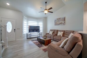 A living room with a flat-screen TV, a ceiling fan, a sofa, and a coffee table. - The Boise Retreat Spacious Home, Game Room! (Boise)