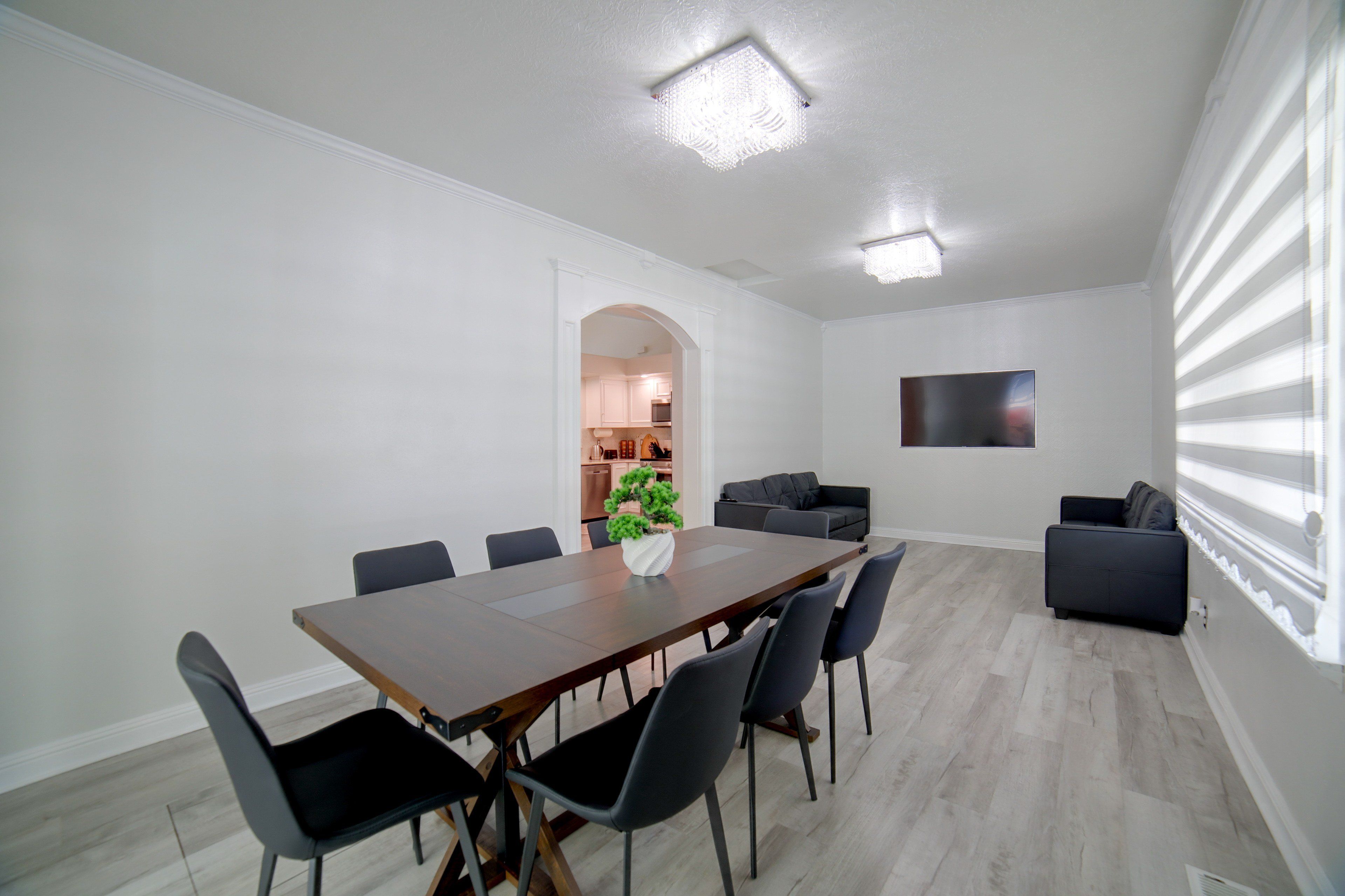 A modern dining area with a wooden table, black chairs, a potted plant, and a television on the wall.