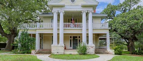 A two-story building with a central entrance, flanked by large columns, and a balcony with railings.