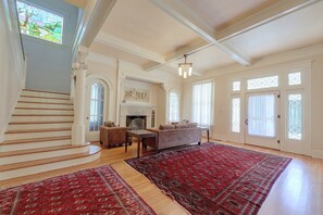 Uma sala de estar ampla com lareira, escada e um tapete vermelho grande.
